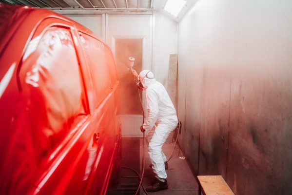 automotive industry manufacturing - mechanic engineer using spray gun and painting a red car