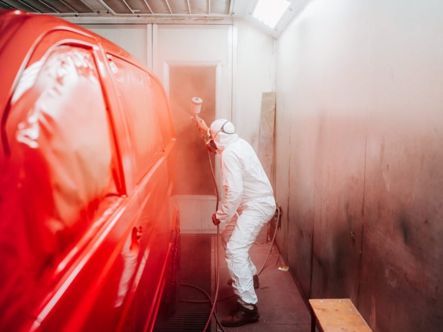 automotive industry manufacturing - mechanic engineer using spray gun and painting a red car