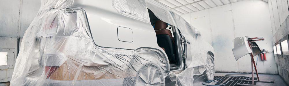 Car in a coating room ready for painting Silver van protected with plastic film from dirt in a spray booth before the start of paint work