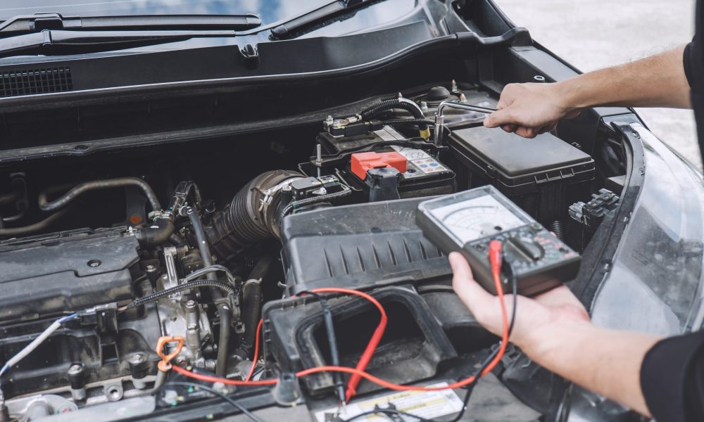Services car engine machine concept, Automobile mechanic repairman hands repairing a car engine automotive workshop with a wrench and digital multimeter testing battery, car service and maintenance.